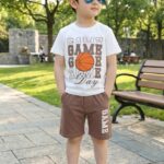 A boy in TrendWale "Game Day" white cotton tee and chestnut brown shorts with side typography.